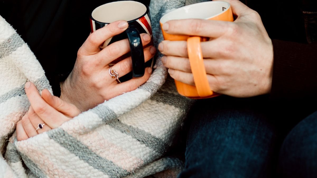 Two people wrapped in a blanket holding mugs, perfect for a cozy scene.