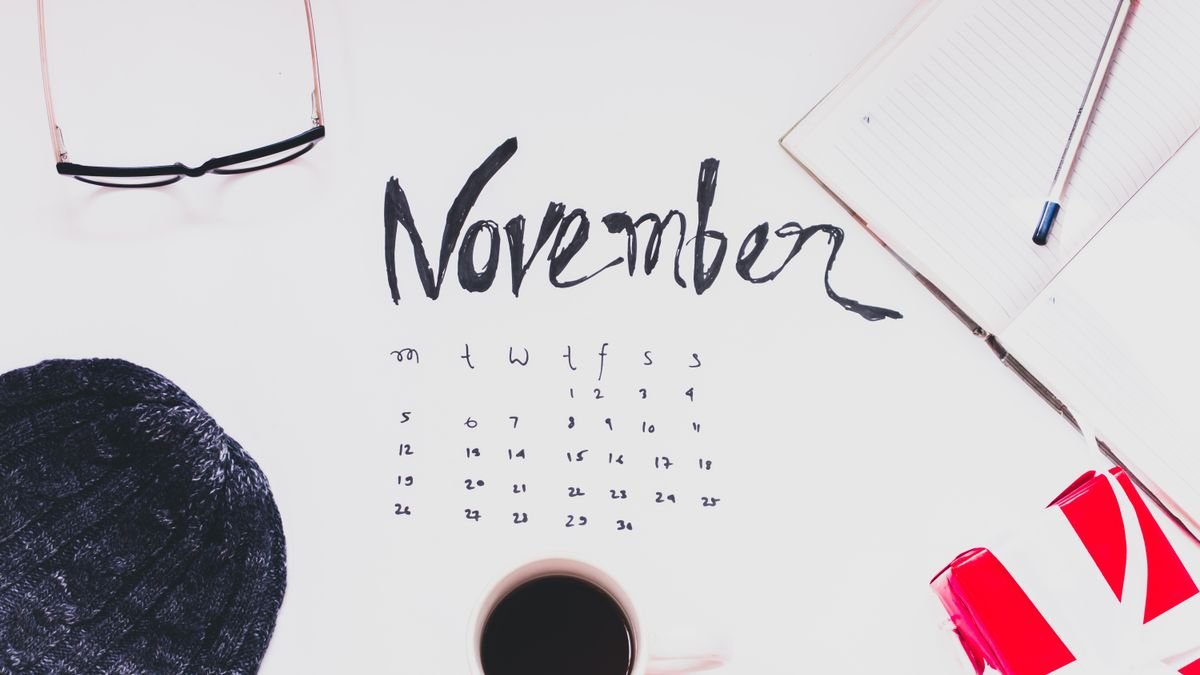 Flat lay of a November calendar with cozy autumn accessories, warm sweater, and hot coffee.