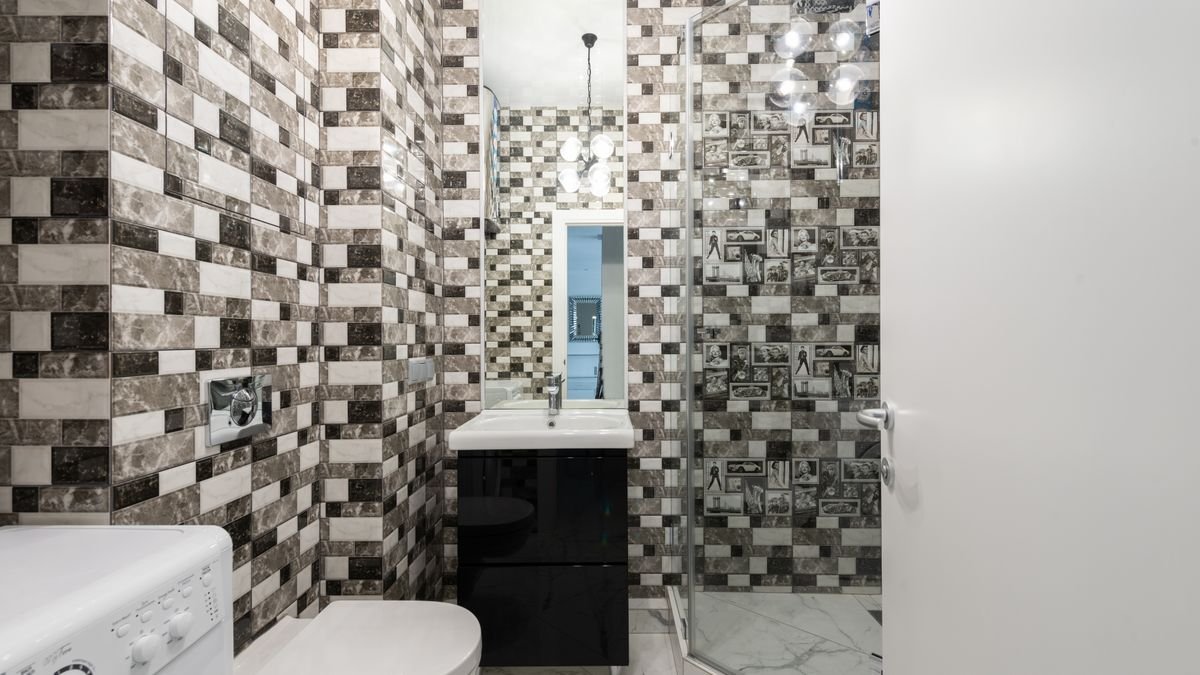 Interior of bright washroom with washing machine near toilet next to shower and sink with tap