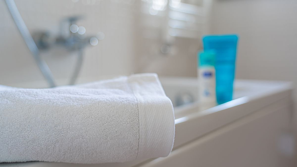 A neatly folded white bath towel on a bathtub edge with blurred bath products in the background.