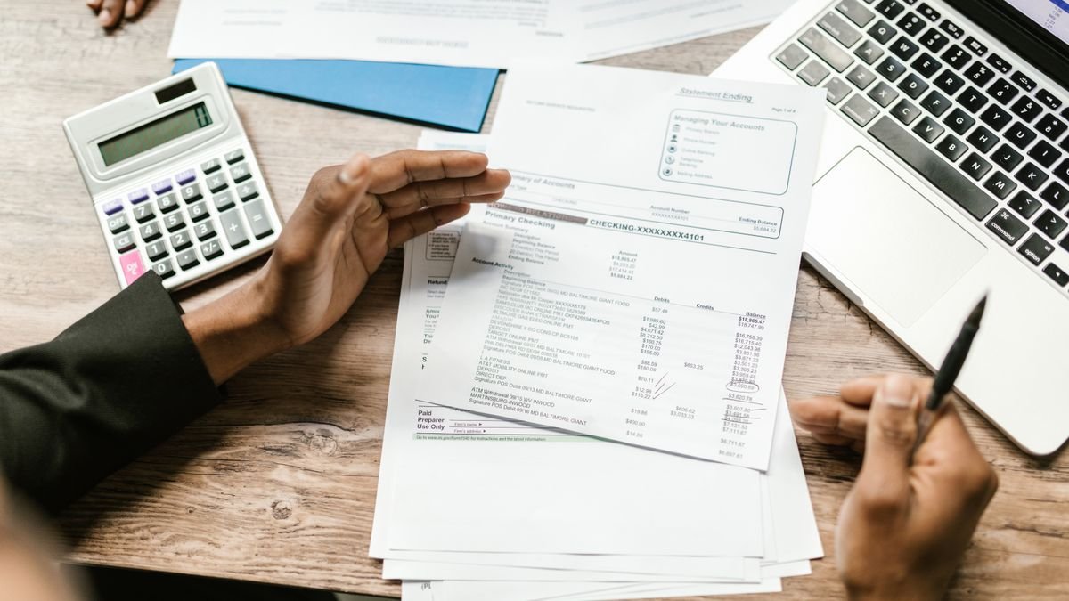 Hands holding financial documents with calculator and laptop on office desk, business analysis scene.