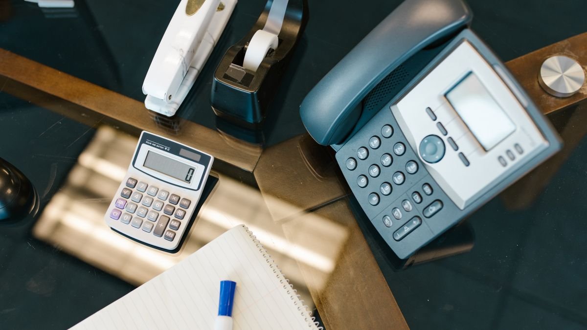 A neatly arranged office desk with a calculator, phone, stapler, tape, and notepad.