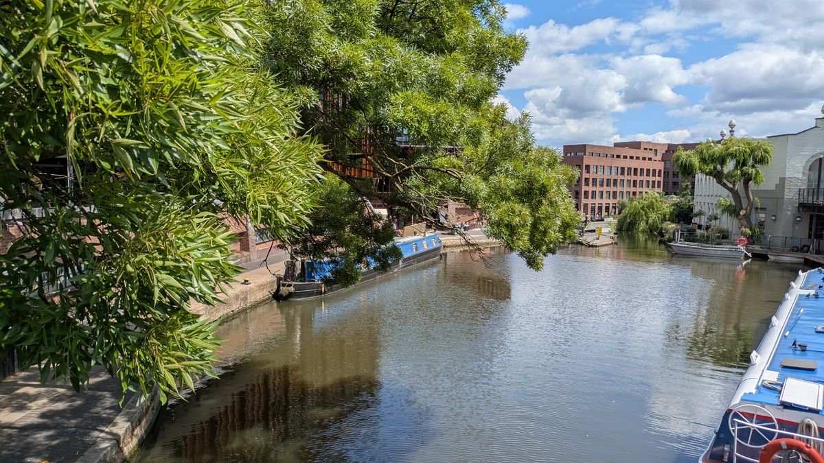 Scenic view of a tranquil canal with moored boats and lush greenery in London under a clear blue sky.