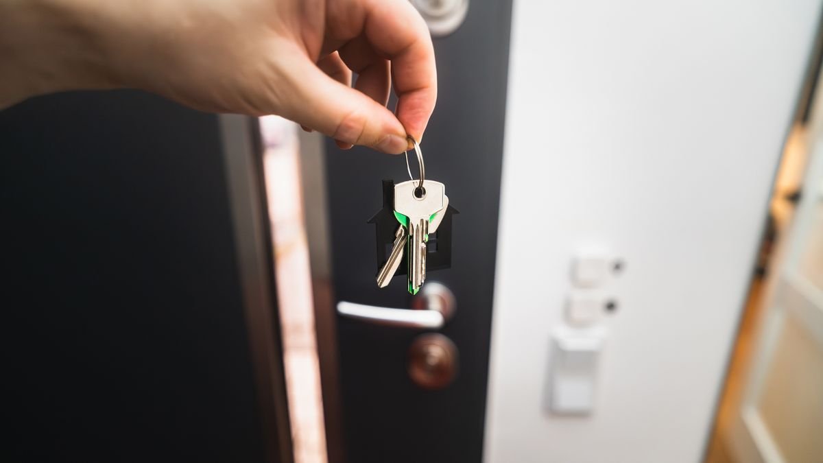 Close-up of a hand holding keys in front of an open door, symbolizing new homeownership.