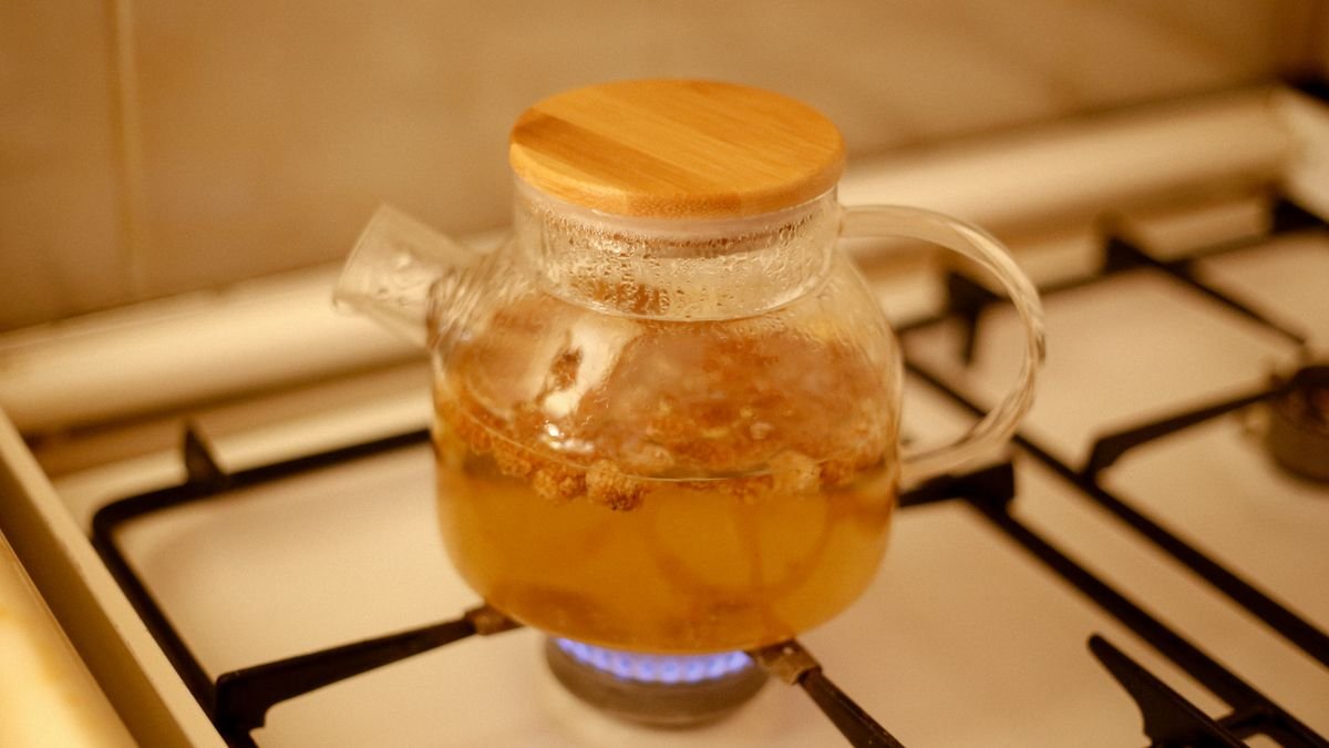 A glass teapot brewing herbal tea on a kitchen gas stove with a warm ambiance.