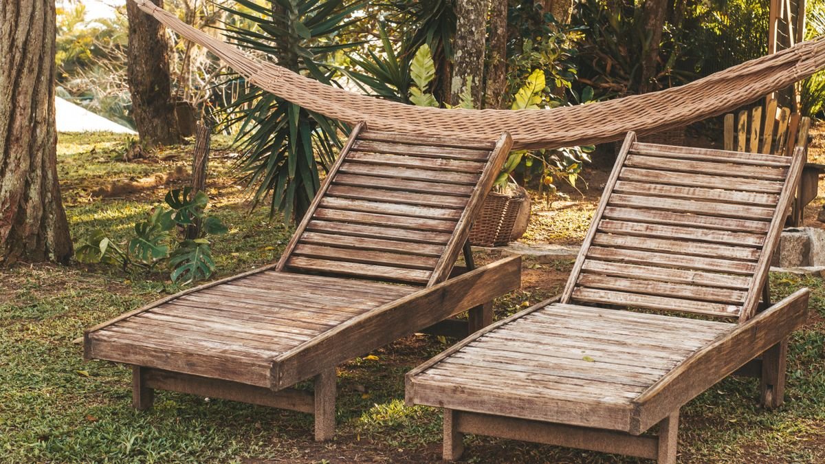 Peaceful garden scene featuring wooden loungers and a hammock under trees, perfect for relaxation.