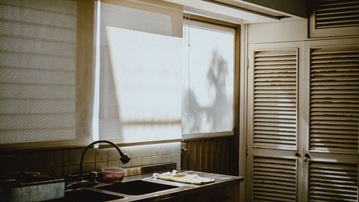 A warm kitchen interior showcasing natural daylight through window blinds and rustic cabinetry.