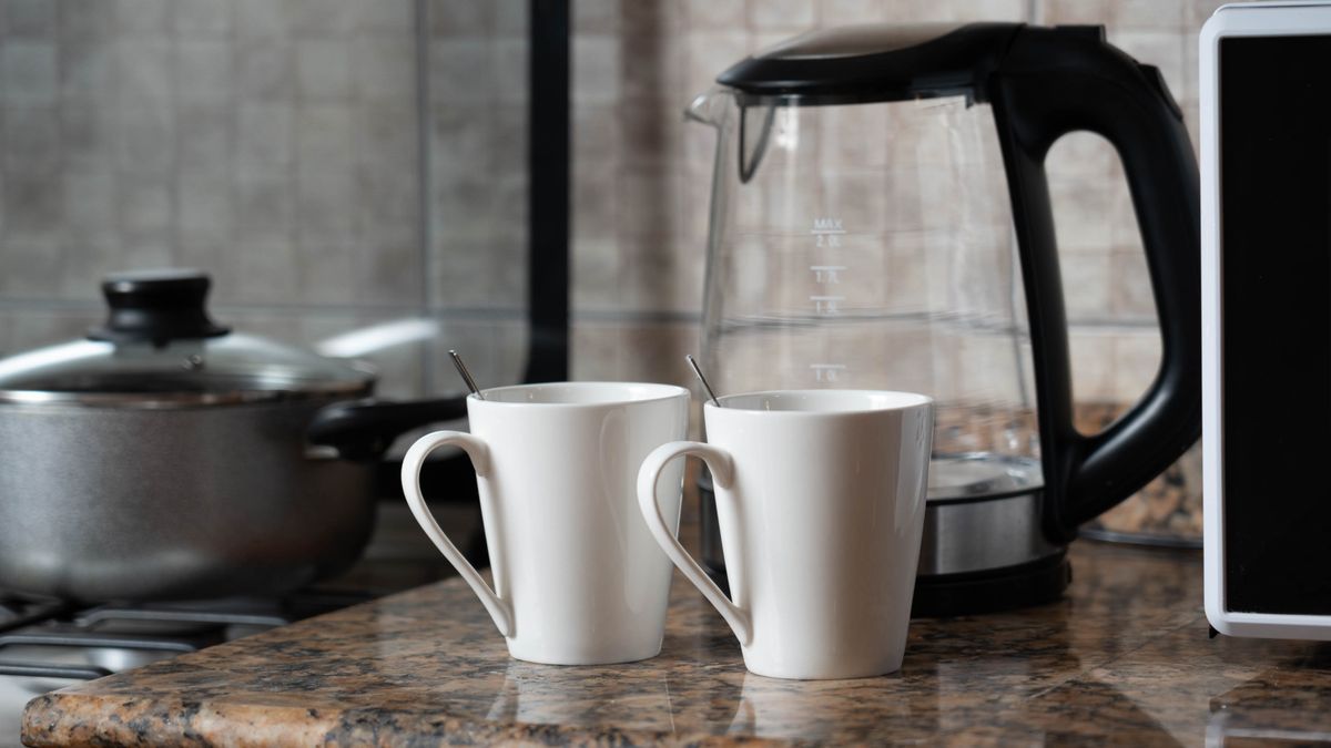 A warm indoor shot of two coffee mugs next to a kettle on a stylish kitchen counter.