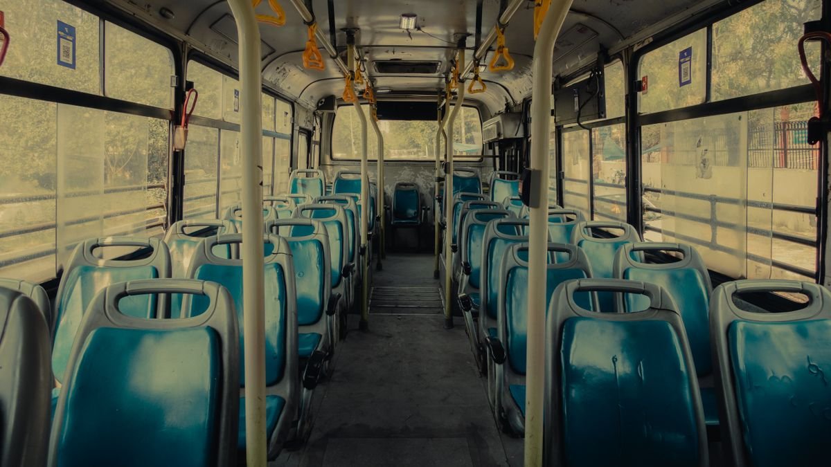 View of an empty public bus interior with blue seats and yellow handrails.