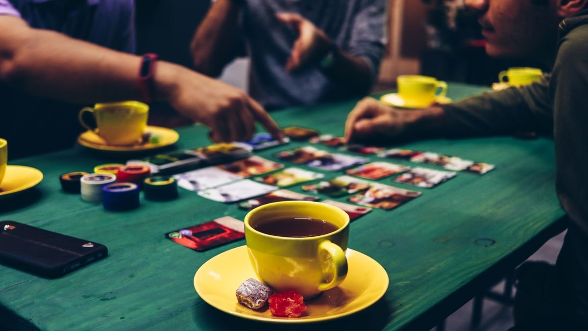 Adults enjoying a board game with tea and snacks in a cozy indoor setting.