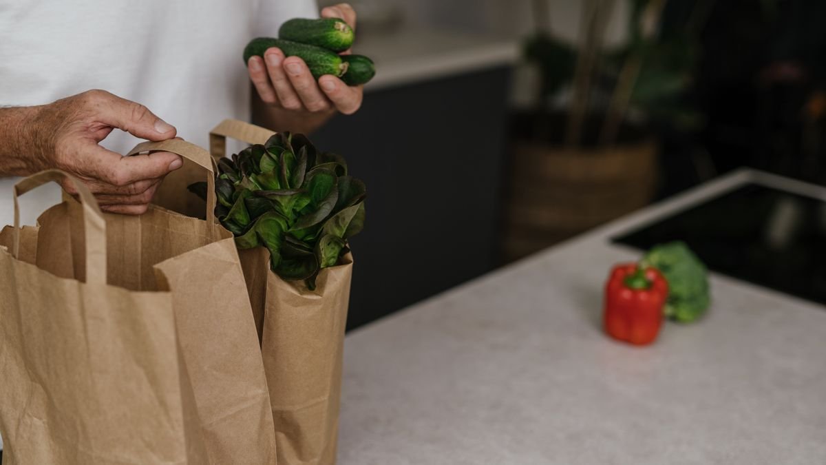 A person placing fresh vegetables into a paper bag on a kitchen counter. Vibrant and healthy organic ingredients.