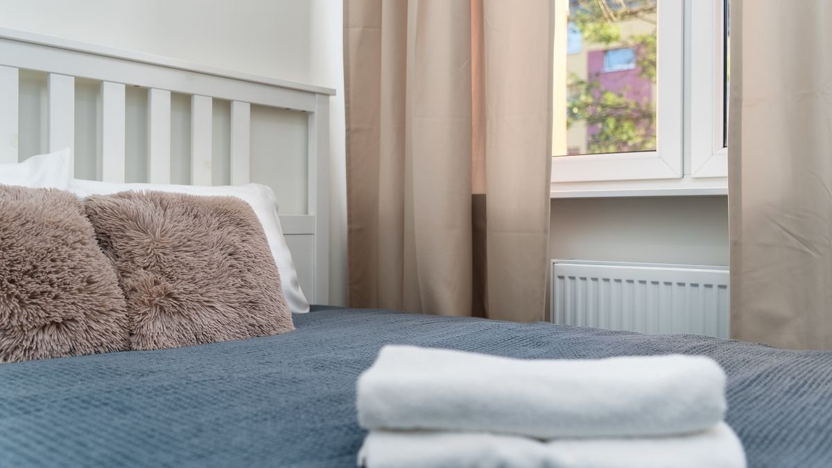 Cozy bedroom with fluffy pillows and folded towels by a sunlit window.